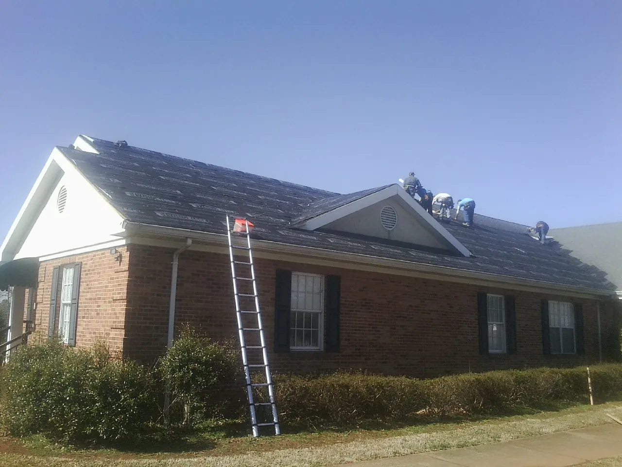 Crew tearing shingles off a brick ranch roof with a ladder set — Metal Roof Repair work by our crew in Westerville