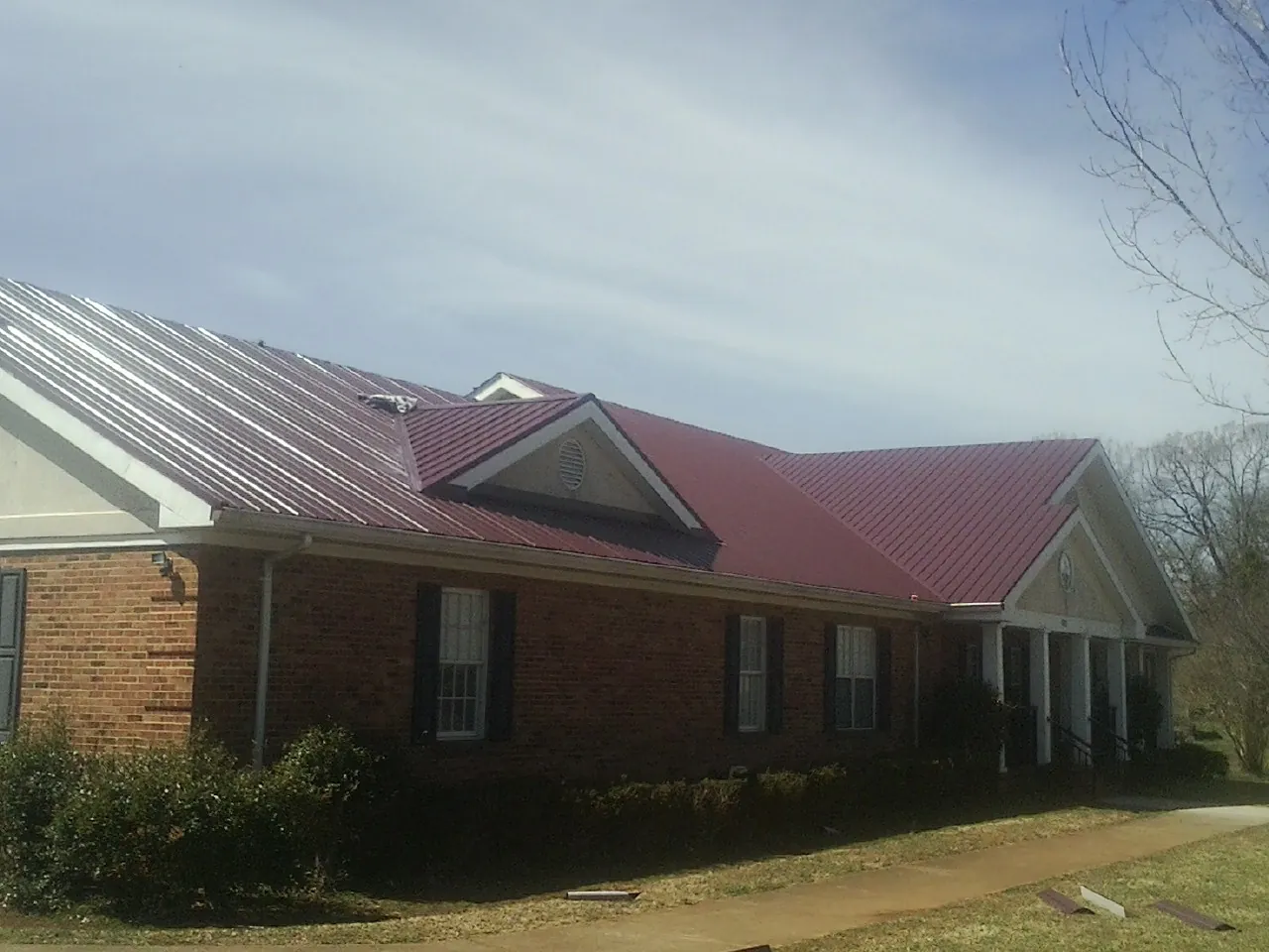 Red metal roof with gabled entries on a long brick building, from a Hail Damage Roof Repair job in Westerville