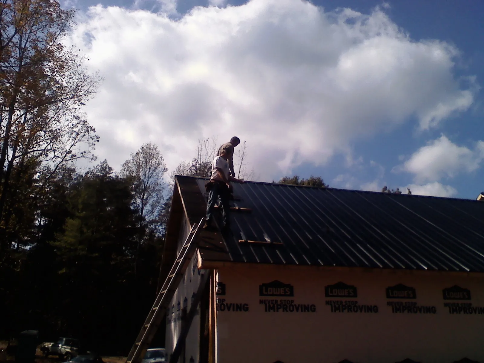 Roofer fastening dark metal panels high against a cloudy sky, from a Roof Inspection job in Westerville